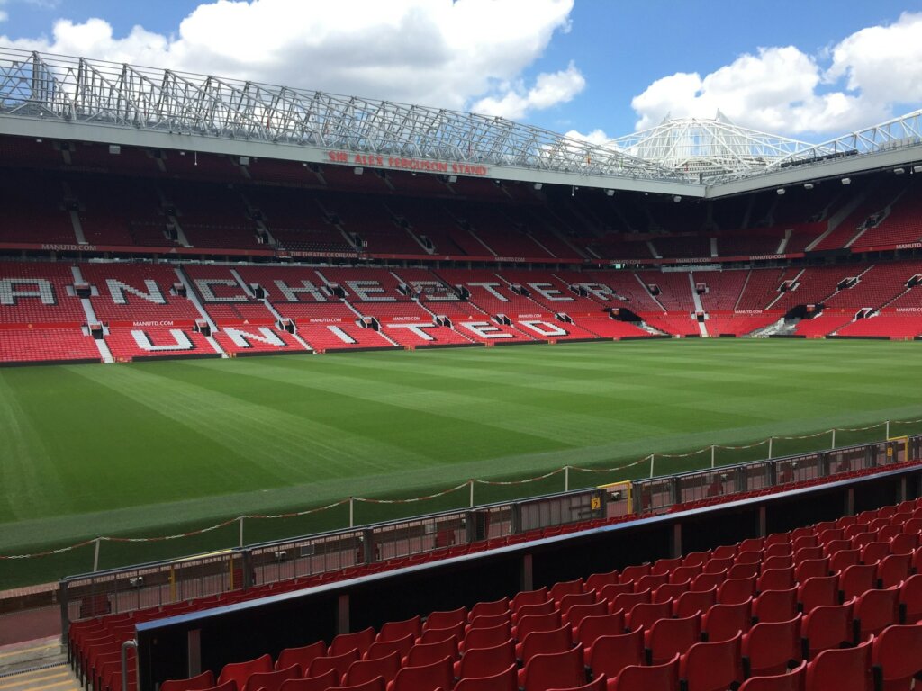 an empty stadium with red seats and a green field Old Trafford