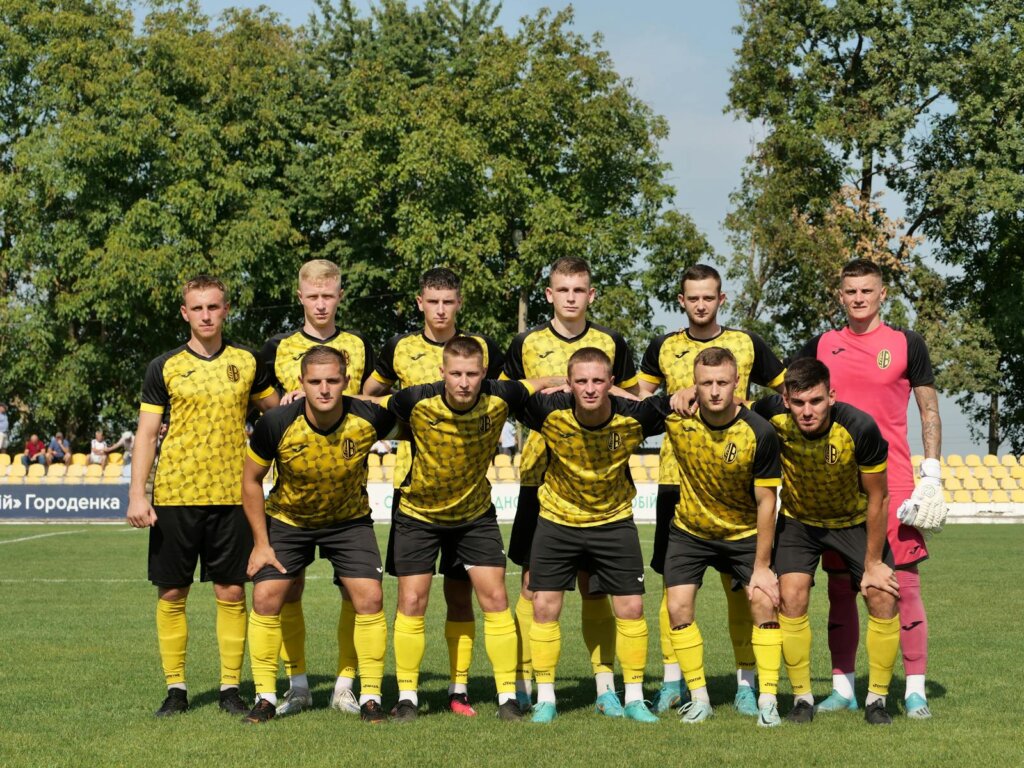 A young men's soccer team in yellow and black uniforms posing on the field before a match.