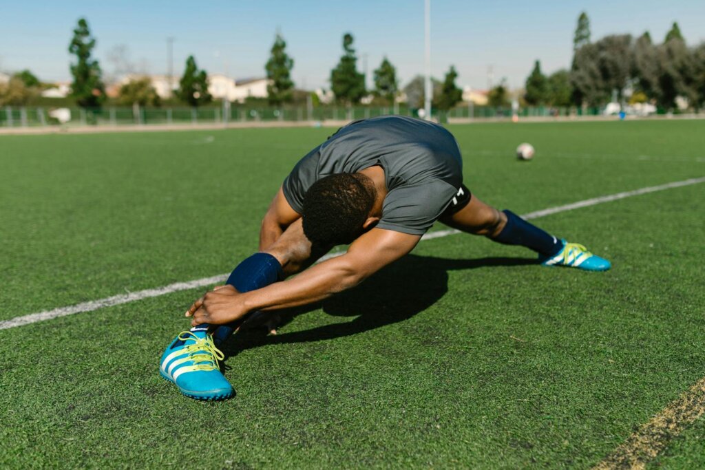 Black male athlete stretching on a soccer field, showcasing flexibility and athleticism.