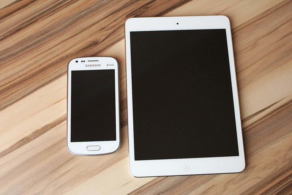 A white smartphone and tablet placed on a wooden table, showcasing technology contrast.