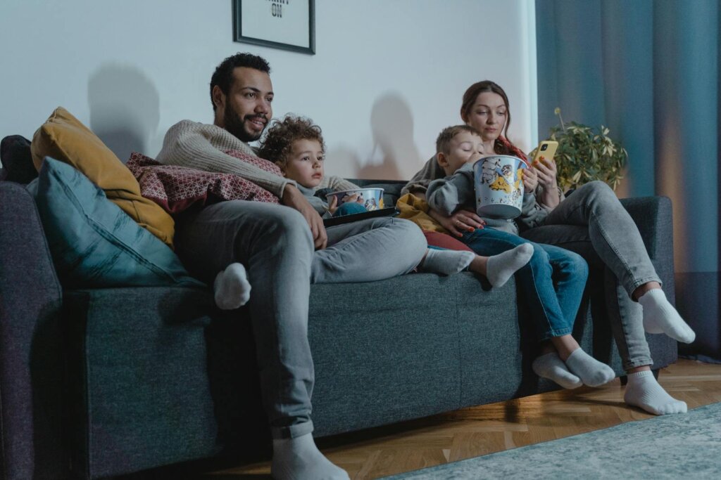 A family of four enjoys a cozy evening on the sofa, bonding over movies and popcorn indoors.